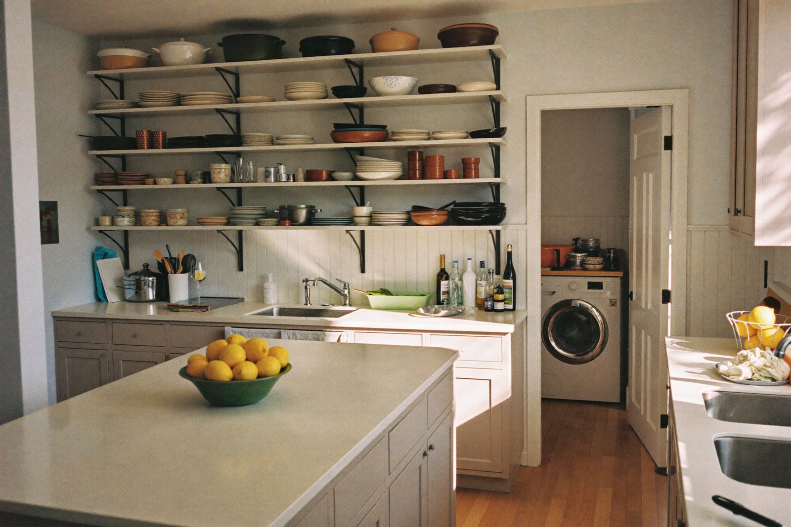 A stocked shared kitchen with open shelving and a washing machine through the doorway