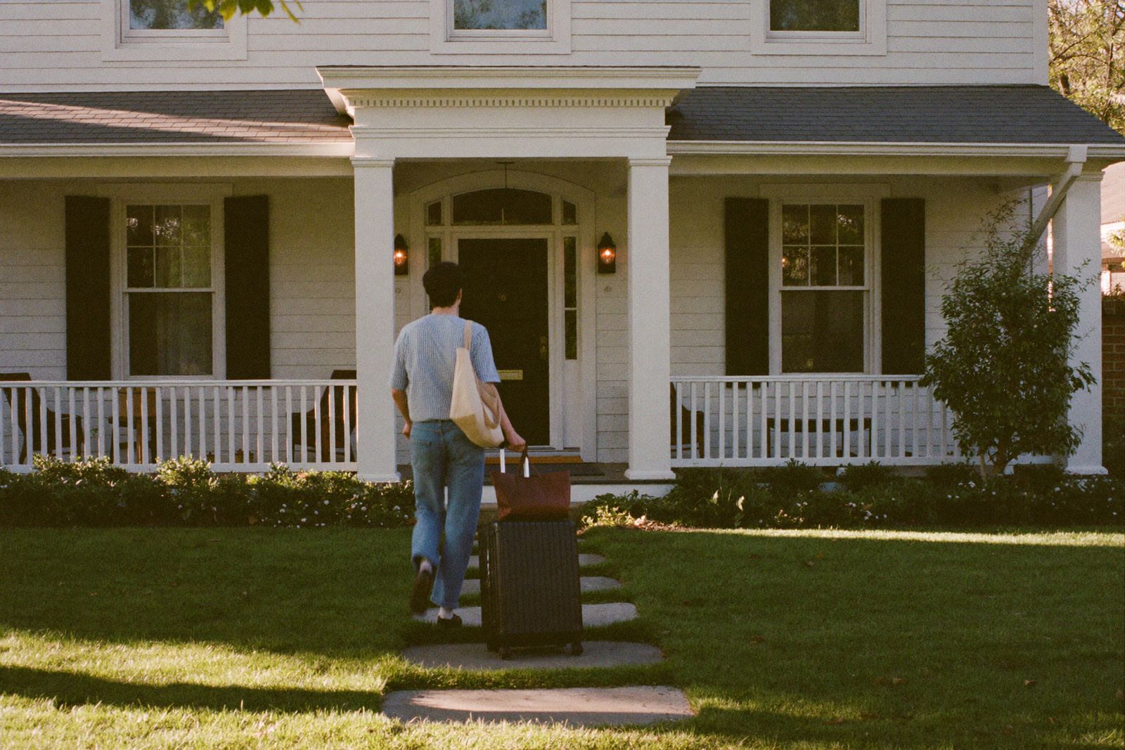 A guest wheeling a suitcase up the front walk of a white house with a wide porch