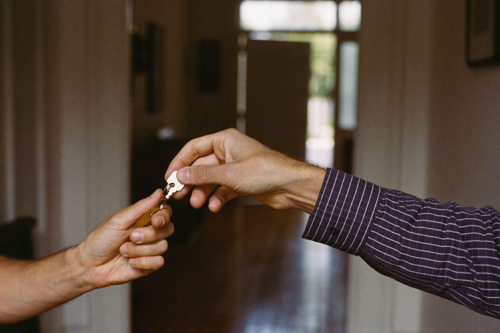 One hand passing a house key to another in a sunlit hallway