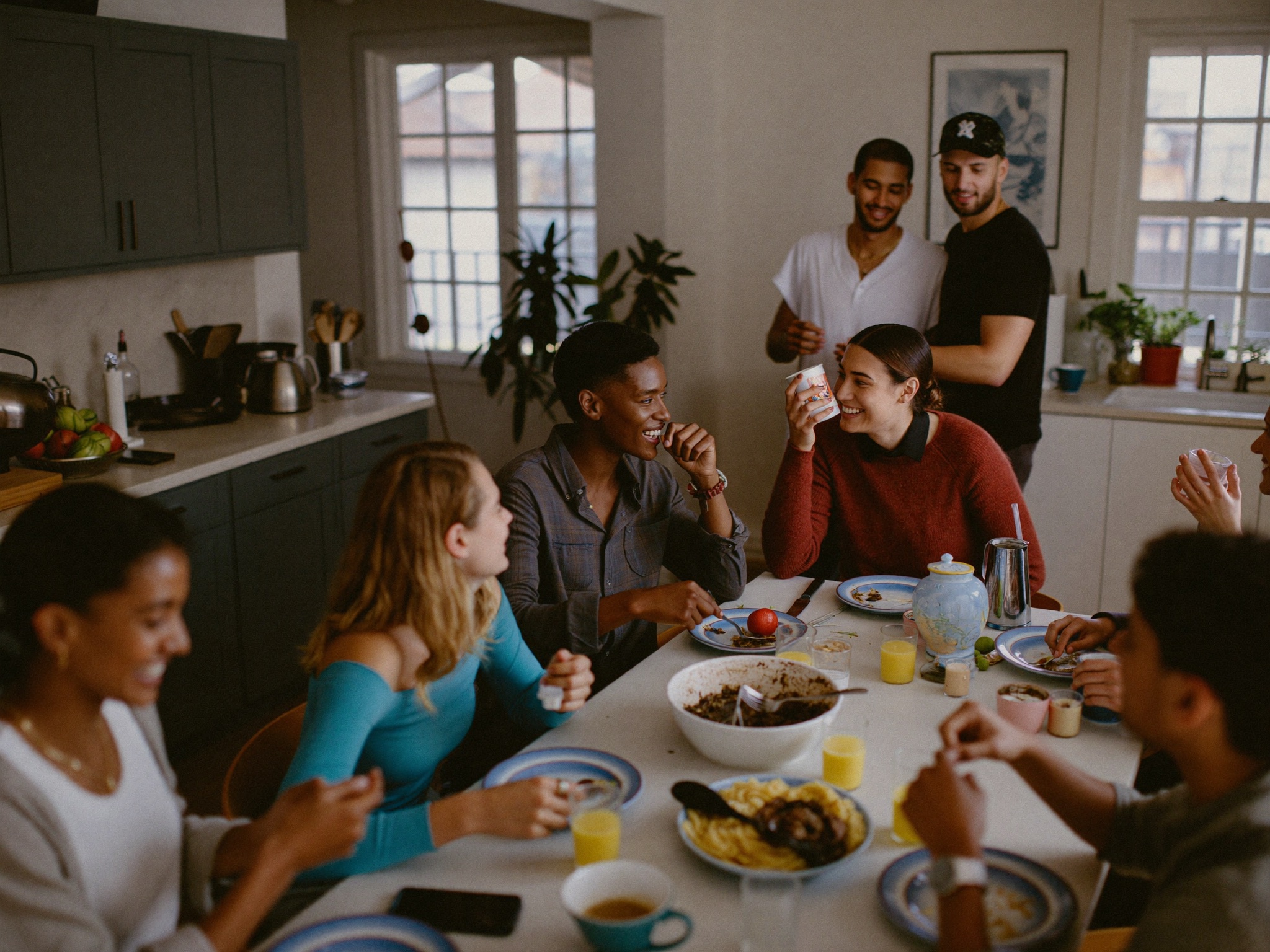 A happy group of co-living housemates cooking and laughing together in a bright shared kitchen.