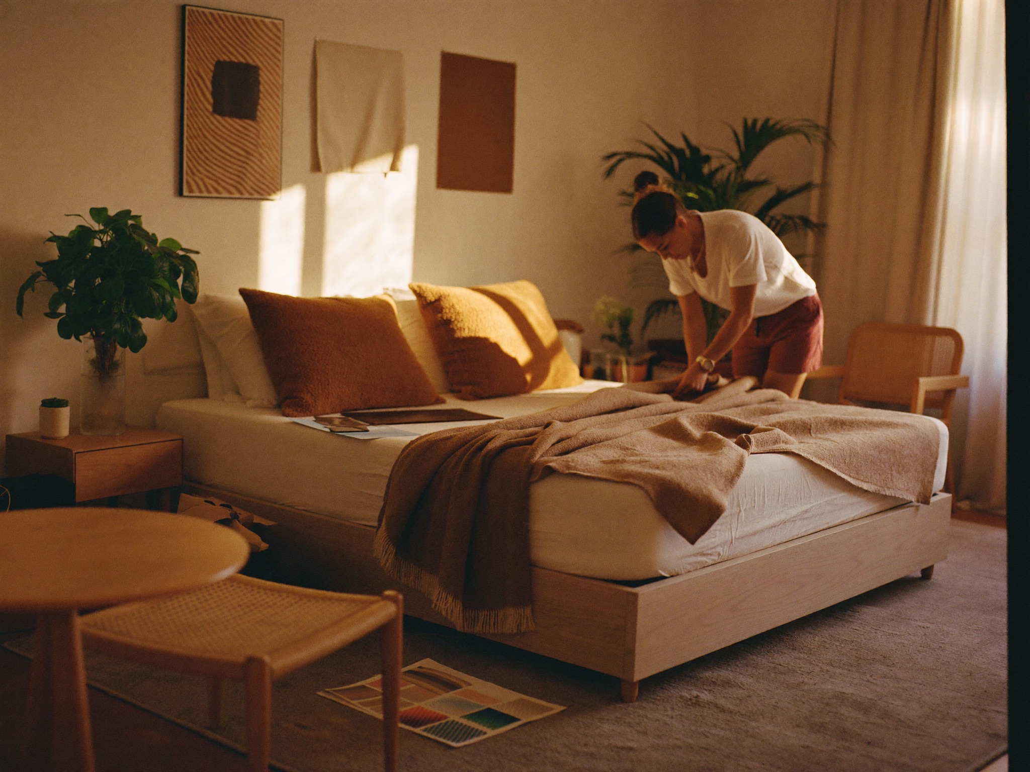 A designer styling a freshly furnished boutique bedroom with warm textures and plants.