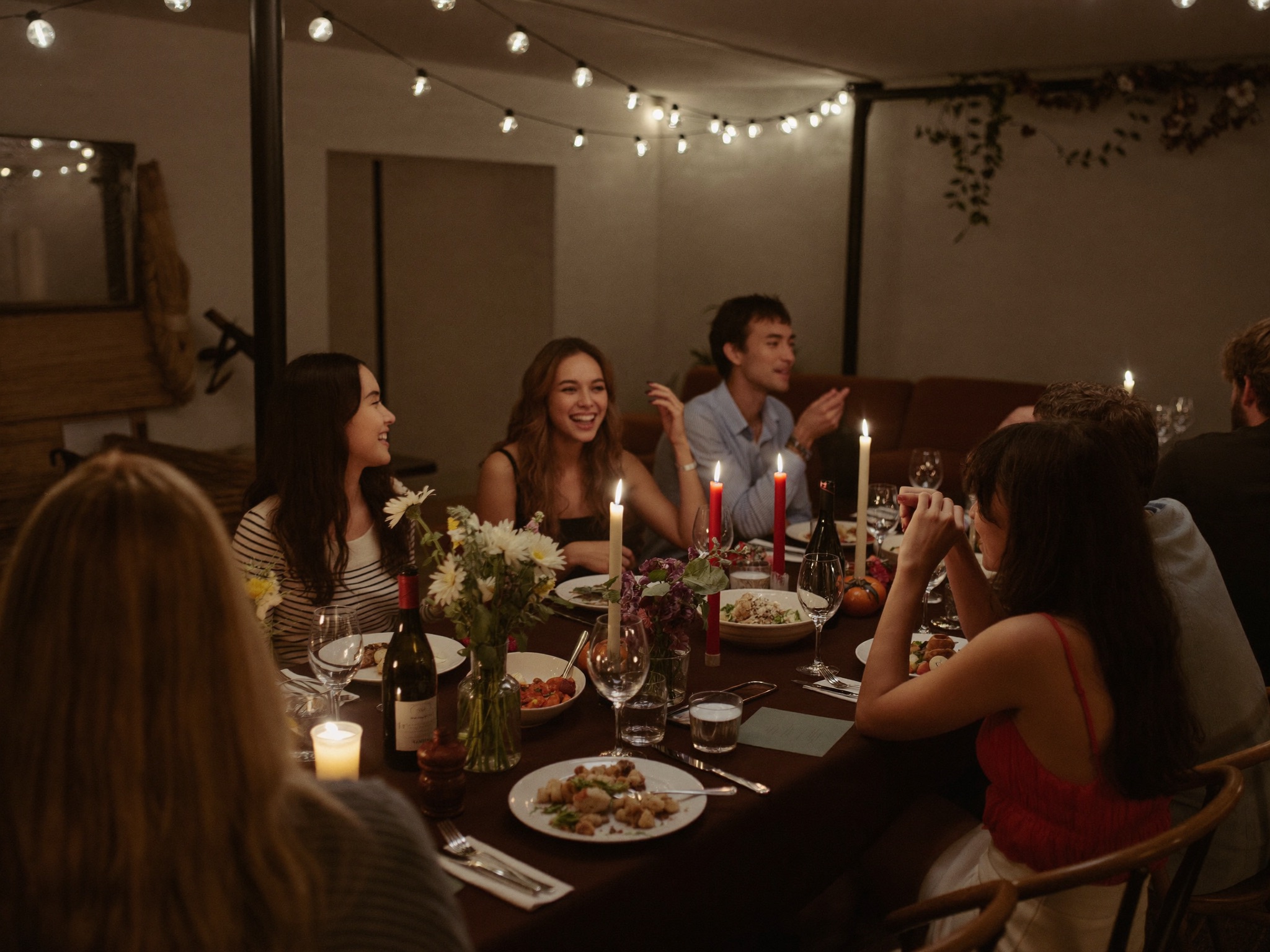 An intimate string-lit evening gathering with a beautifully set table and happy guests.